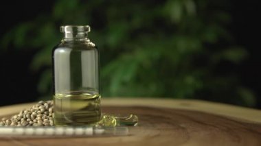 Cam kavanoz şişesine, oral yönetim için tıbbi kenevir cbd yağıyla aşırı yakın çekim. Ağaç çemberi ağaç halkası masasında, şırınga, kenevir tohumu ve yeşil marihuana bitkisi arka planında.