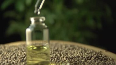 Kenevir bitkisinin biyolojik ve ekolojik yağına ilaç katan makro yakın plan. Kenevir tohumlarıyla dolu tahta masanın üzerindeki küçük kavanozdaki bitkisel cbd yağı. Organik ilaç konsepti.