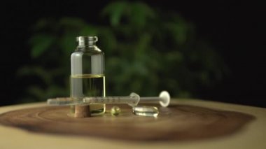 Oral kullanım için şırıngada kenevir yağı ve küçük cam kavanoz şişesi. Yağ kapsülleri tedavi için bir seçenektir. Esrar arka planda kalır. Ve ahşap yuvarlak ağaç halka masası..