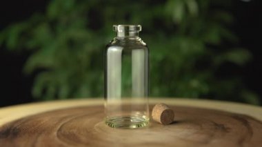 Cam kavanoz şişesini ağız sağlığı için kenevir cbd yağı karışımıyla dolduruyorum. Arka planda yeşil marihuana bitkisinden yapılmış. Ağaç çemberi halkası masasında çeşitli organik ilaçlar var..