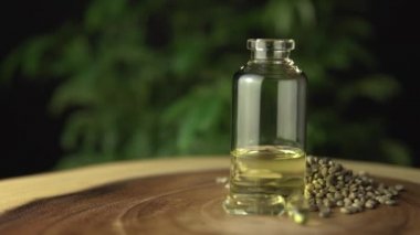 Cam kavanoz şişesinde tıbbi kenevir cbd yağ yoğunlaştırılmış reçine var. Oral yönetim için taşıyıcı yağla sulandırılmış. Ahşap masa ve yeşil kenevir bitkisi arka planı.