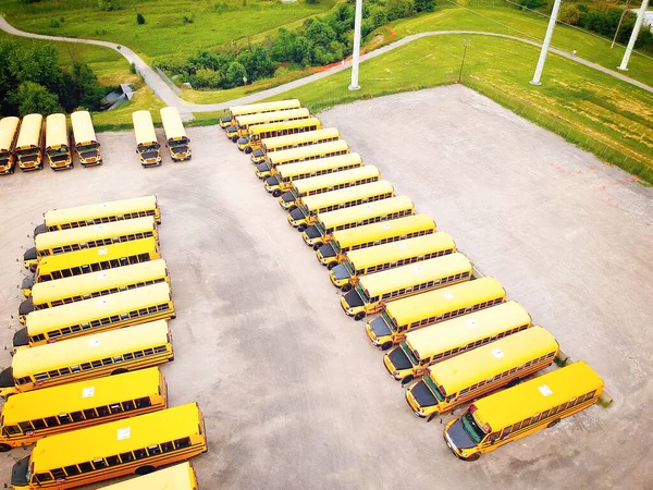 School bus vehicles ready for school educational season. Parking lot of school busses. Drone aerial view of parking yard with yellow tracks and evening sky ready to pick up and drop off young college students. Back to school concept.