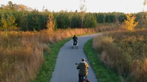 Gezginler, kadın ve erkek bisiklete biniyor ya da sonbahar ya da sonbahar parkında gün batımında bisiklet sürüyor. Tatil etkinliği, yukarıdan turuncu, sarı ve yeşil ağaçlar görünüyor.. — Stok video