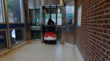 Toronto, Ontario, Kanada - 10 Eylül 2019: Şehirde elektrikli scooter kullanan kadınlar. Asansörü devre dışı bırakmak için girişe giriyorum. Ekolojik güç nakli. Etkin yetişkin yaşam tarzı.
