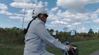 Güneşli yaz gününde parkta elektrikli bisiklete binen köylü kadın. Yan taraftan yakın çekim. Doğal ışıklandırma. Uzaktan kumandanın ve kabloların görüntüsü. Yaz tatili yaşam tarzı.