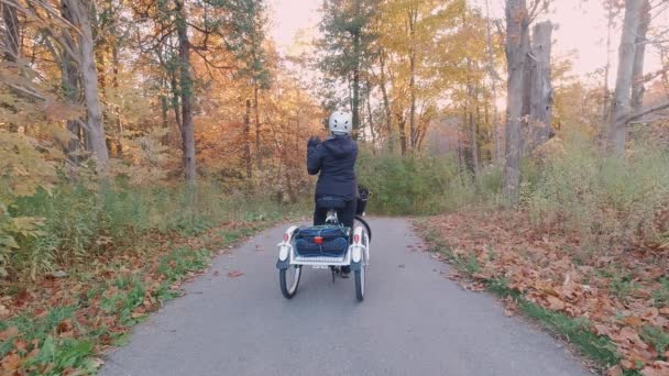 여행하는 여성은 해 가 지는 숲 속 공원에서 전기 자전거, 전자 자전거 또는 자전거를 타는 동안 셀카나 숲의 사진을 만든다. 자연의 번개를 뿌리는 거야. 북아메리카에서의 활동적 인 관광. — 비디오
