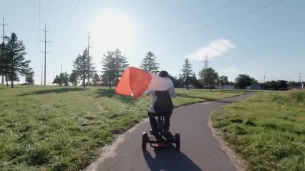 Kvinnor rider en elektrisk skoter i stadsparken samtidigt som de håller kanadensiska flaggan i vinden. Lycklig kanadensisk medborgare som kör ekologisk miljömedveten krafttransport. Aktiv livsstil för vuxna. — Stockvideo