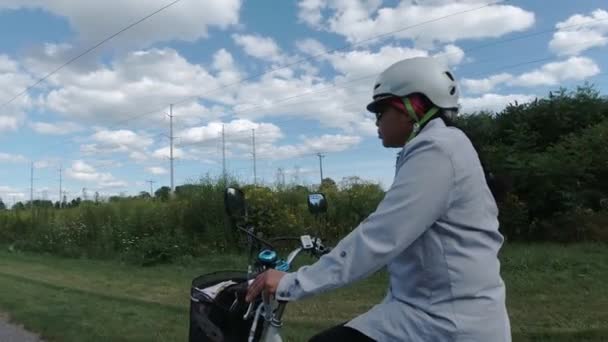 Vrouw in de helm paardrijden elektrische fiets in het park in de zonnige zomerdag. Van dichtbij geschoten vanaf de zijkant. Natuurlijke verlichting. Het uitzicht op de afstandsbediening en de bedrading. Zomer vrijetijdsbesteding. — Stockvideo