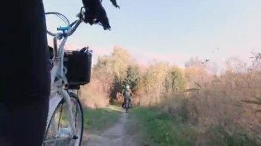 Orman parkında günbatımında elektrikli bisiklete binen birkaç yolcu, E-bisiklet ya da bisiklet. Sonbahar doğası, doğal şimşek. Aktif turizm, Kuzey Amerika 'da turuncu yaprak parkında gezintiler.