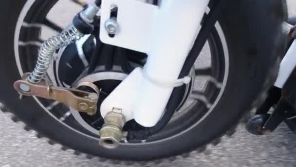 Közelkép egy első motor kerék forog a motorháztető alatt, miközben elektromos robogó. Oldalról nézve. Modern alternatív közlekedés, népszerű mobilitási lehetőség. — Stock videók