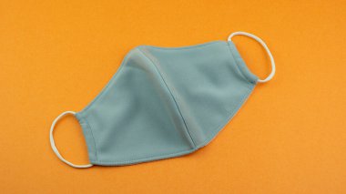 Virüs ve tozdan korunmak için tıbbi olmayan yüz maskesi. Kanunen zorunlu maske ve Covid 19 salgınından dolayı Yeni Normal Sosyal Mesafe kavramı. Turuncu arkaplan. 