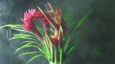 Ormandaki yağmur sisinde bir buket tropik egzotik çiçek. Yağmur ormanları bahçesinden Heliconia Rostrata çiçek aranjmanının yakın çekimi. Cennet Kuşu ve Istakoz Pençesi eğreltiotu ile yaprak arkaplan.