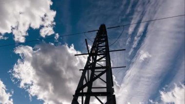 Endüstriyel yeşil enerji şebekesinin hızlandırılmış elektrik şebekesi üzerinde mavi bulutlar olan verici silueti. Yüksek voltajlı güç hattı ile günbatımı arkaplanı zamanlaması.