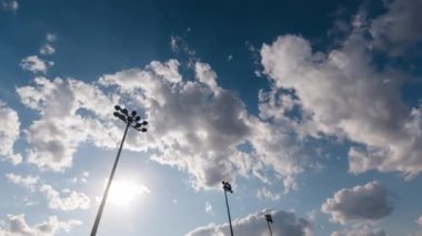 Gün batımı ve yaz bulutlarına karşı bir futbol stadyumunun ışık kulesiyle zaman geçirmek. Sinema gibi hızlı ve pürüzsüz bir gökyüzü hareketi. Futbol stadyumunun el fenerleri ve akşam süreleri.