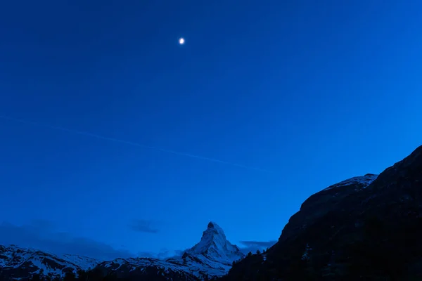 Very beautiful nature of  Matterhorn mountain , Switzerland Alps view from Zermatt at night time with moon and airplane contrail