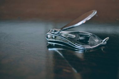 Tahta masadaki tırnak kesiciyi kapat. Metalden yapılmış çivi kesicisi ve yansımasıyla ahşap masanın üzerindeki parlak tabakayla kaplanmış..