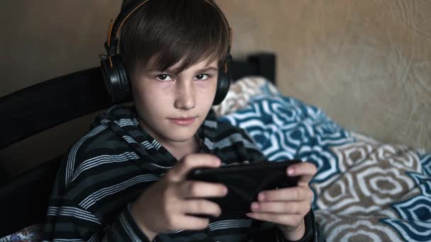 一个快乐的少年男孩的肖像躺在床上 用智能手机和耳机睡在家里听音乐 休息和技术概念 — 图库视频影像