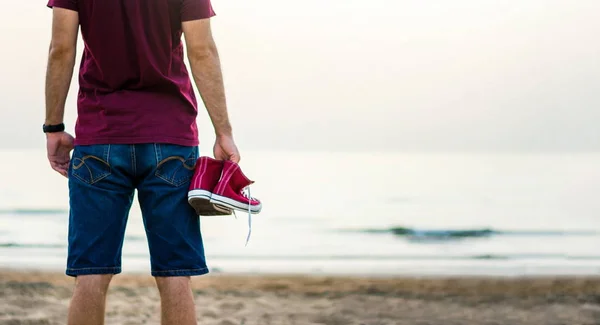 Uomo Che Tiene Scarpe Ginnastica Sulla Spiaggia Crepuscolo — Foto Stock