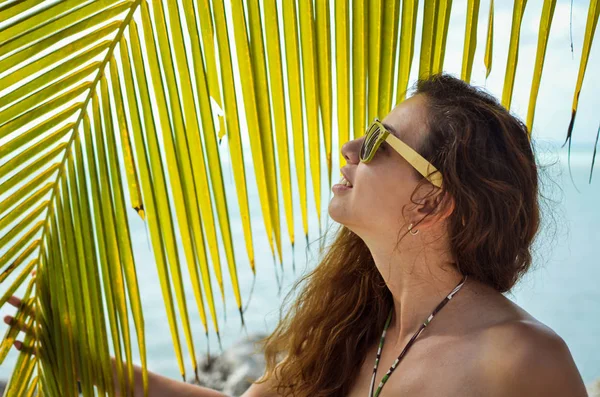 Девушка в солнечных очках позирует рядом с пальмой — стоковое фото