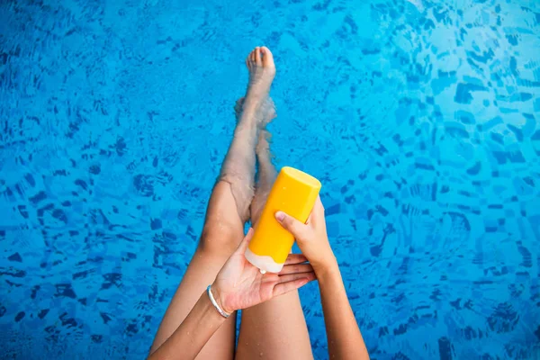 Девушка, использующая солнечный лосьон в бассейне — стоковое фото