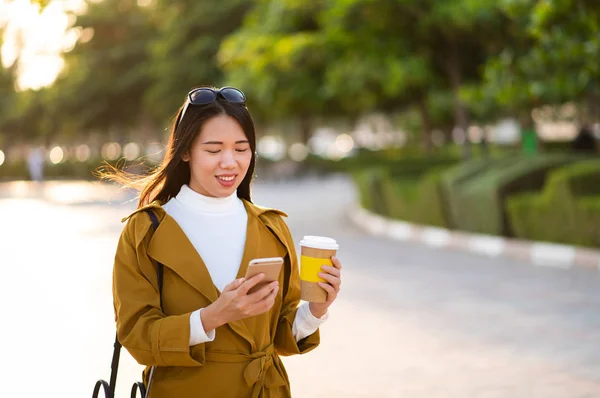Žena má šálek kávy a použití telefonu venku — Stock fotografie