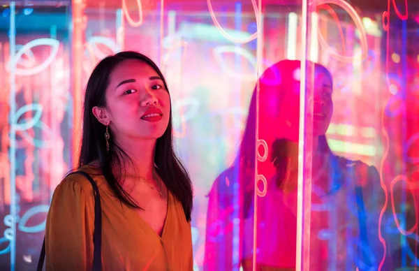 Asian woman portrait lit up by neon illuminated mirrors at night