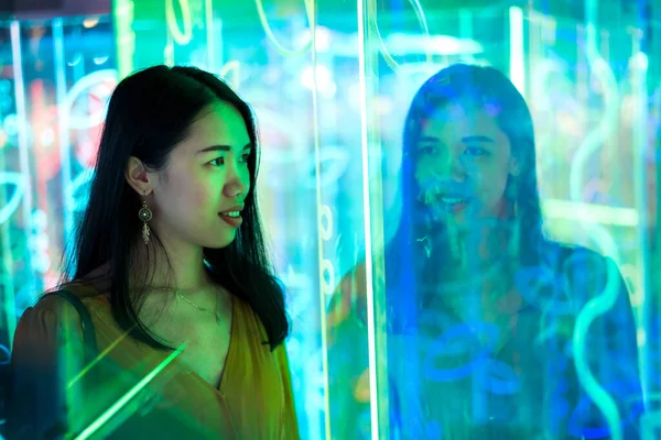 Asian woman portrait lit up by neon illuminated mirrors at night