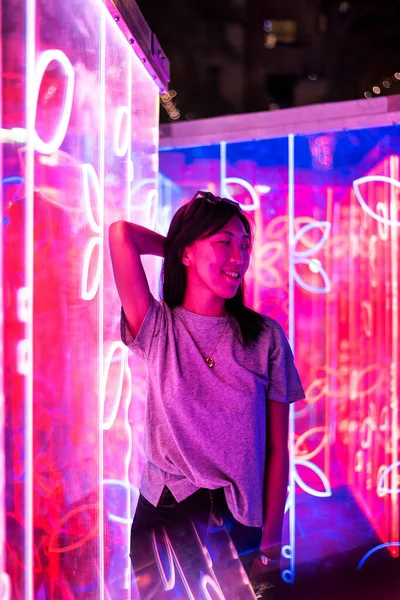 Asian woman portrait lit up by neon illuminated mirrors at night