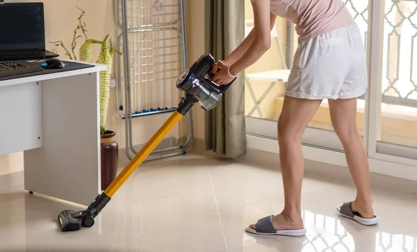 Woman vacuuming the living room with a cordless vacuum cleaner. House cleaning and maintenance abstract