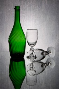 Canlı yeşil şişe ve şeffaf camdan yapılmış iki bardak. Arka plan gümüşi..
