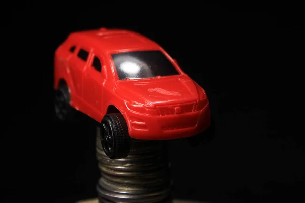 Saving money for a car. Banking, fast. Toy car and coins on black background. Miniature red car model on growing stack of coins. Finance and car loan.