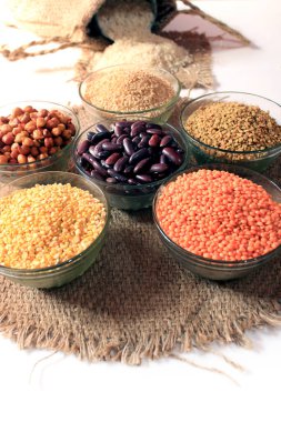 Beyaz arka planda izole edilmiş küçük çuvaldan pirinç. Beyaz arka plandaki bir kasede farklı renkte nabız. Chick Pea, Red Kidney, Lentil, FenuGreek Seed, Wheat Dalia, Pigeon Pea