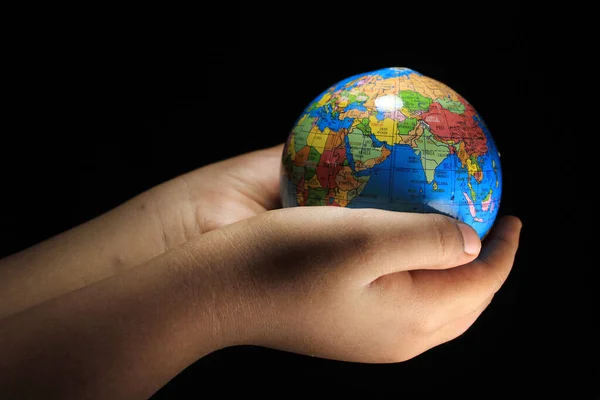 Child hands holding the Earth globe on black background. Earth globe isolated on a black background. School globe on black background.