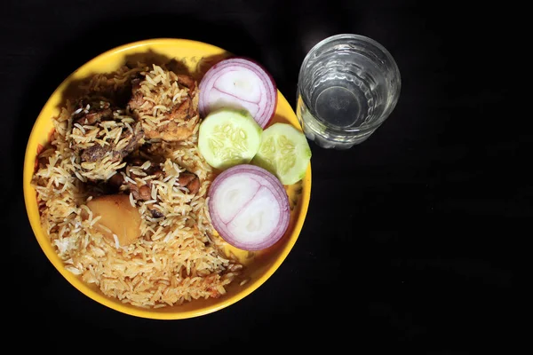 おいしいインドの鶏Biriyani黒の背景に隔離された黄色のプレート上に インドのチキンBiriyaniキュウリとカレー食品 玉ねぎ インドのチキンティッカ ビリヤニカレー — ストック写真