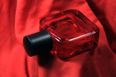 Kırmızı renkli erkekler, kırmızı ipek arka planda izole edilmiş parfüm şişesi. Siyah şapkalı kırmızı parfüm şişesi, doğal sprey..