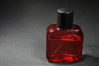Kırmızı renkli erkekler siyah ipek arka planda izole edilmiş parfüm şişesi. Siyah şapkalı kırmızı parfüm şişesi, doğal sprey..
