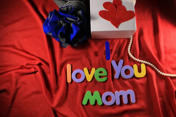 Colorful letters with I love you mom isolated on red cloth background. I love you mom spelled with colorful letters and red heart for mothers day. Mother\'s day gift box.