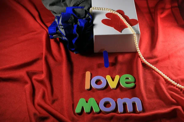 Colorful letters with I love mom isolated on red cloth background. I love mom spelled with colorful letters and red heart for mothers day. Mother\'s day gift box.