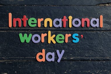 Uluslararası İşçi Günü metni ahşap arka planda kırmızı renkte ve inşaat onarım araçlarıyla. İşçi bayramı tabelası. Siyah ahşap zemin üzerine yazılmış Uluslararası İşçi Günü metni.