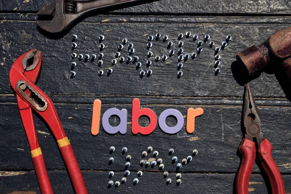 Happy Labor day text in red color on wooden background with construction repair tools. Labor day concept sign. Happy labor day - writing screws.