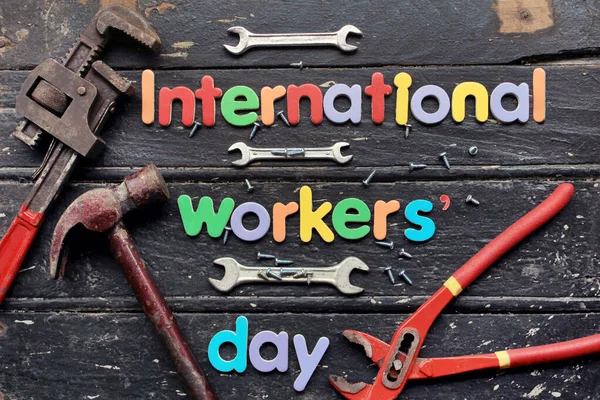 International workers\' day text in red color on wooden background with construction repair tools. Labor day concept sign. International workers\' day text written on black wooden background.