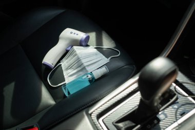COVID-2019 konu, elektronik termometre, maske, siyah araç koltuğunda antiseptik.