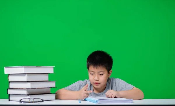 Asian boy doing homework on green screen, child writing paper,  education concept, back to school