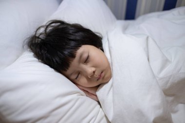 Asyalı çocuk yatakta uyuyor, hasta çocuk.