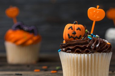 Cadılar Bayramı partisinde kek. Renkli krema, krema ve çikolata ile süslenmiş tatlı. Balkabağı oyulmuş Jack-o-fener ve sopa. Doğal ahşap zemin üzerine çörekler. 