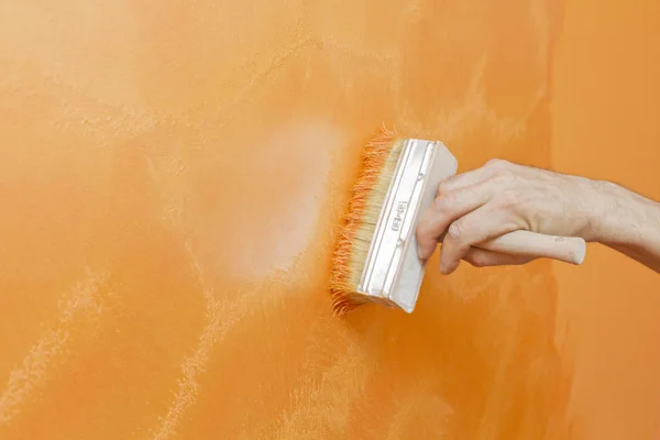 hand of painting worker orange inflicting structural paint on wall