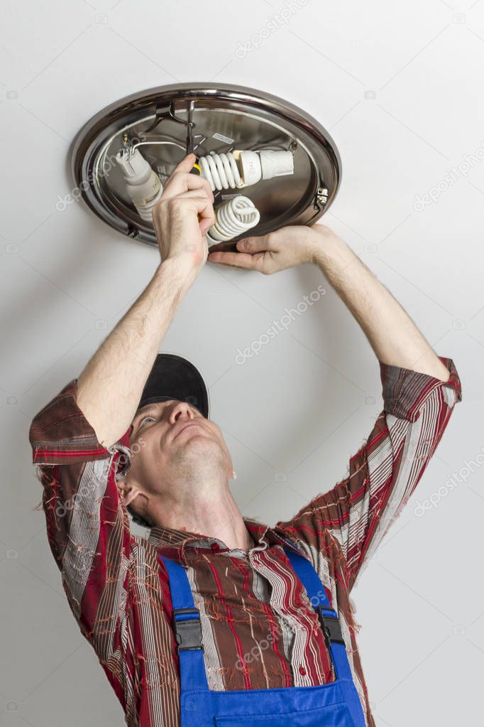 Electrician installing lighting lamp on ceiling of room