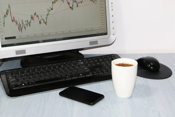 クローズ アップ コンピューター コーヒー カップ スマート フォン 株価チャートのためのモニターのテーブルの上 — ストック写真