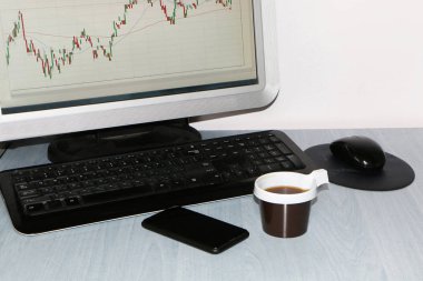 Yakın çekim-masada bir bilgisayar, bir plastik tek kullanımlık fincan kahve, bir akıllı telefon, bir hisse senedi grafiği için bir monitör var