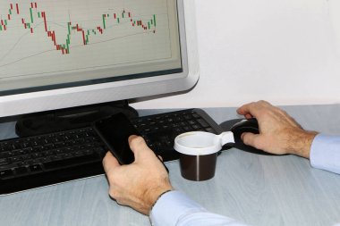 Yakın çekim-masada bir bilgisayar, bir plastik tek kullanımlık fincan kahve, bir akıllı telefon, bir hisse senedi grafiği için bir monitör var